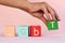 A woman`s hand with rainbow nails lays out the inscription LGBT from cubes. abbreviation LGBT on a pink background.