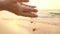 Woman`s hand with soft sand falling on tropical beach.