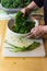 Woman`s hand squeezing kale leaves to break down tough fibers, stripped ribs on cutting board