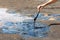 A woman`s hand stirring liquid asphalt with a wooden stick at Pitch Lake, La Brea, Trinidad island, Trinidad and Tobago