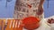 Woman`s hand is stirring orange porridge with spoon in big glass pan on table