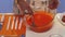 Woman`s hand is stirring orange substance with spoon in big glass pan on table