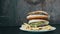 A woman`s hand takes a burger from a large mountain of three delicious juicy burgers with lettuce leaves and cheese