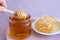 a woman\'s hand takes honey on a wooden stick from a full jar of honey with honeycombs on a plate