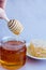 a woman\\\'s hand takes honey on a wooden stick from a full jar of honey with honeycombs on a plate