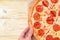 A woman`s hand takes a piece of pepperoni pizza, copy space