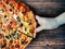 Woman`s hand takes a slice of pizza dark brown background