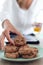 A woman`s hand taking chocolate cookies from a plate while holding an orange juice in the other hand