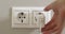 Woman's hand unplugging white power plug into white multiple socket indoors.