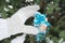 A woman`s hand in a wool knitted mitten holds a Packed gift box in winter against a snow-covered Christmas tree