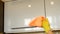 Woman`s hand in a yellow rubber glove cleans the surface of a modern plastic kitchen Cabinet with an orange cloth. The concept of