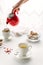 Woman`s hande pouring tea from red teapot, white tea cups, sugar bowl standing on white table