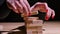 The woman's hands are assembling a tower of wooden bars on the table. Close up wooden puzzle blocks on black background.