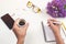 Woman`s hands with coffee on office desk. Workplace with notebook, phone, glasses, pen, lilac flowers, cup of coffee. Flat lay, t