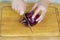 Woman`s hands cutting root ends off red onion