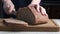 Woman's hands cutting whole grain wheat bread on wooden board.