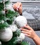 Woman`s hands hanging silver Christmas ball on fir treee