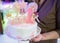 Woman`s hands hold White birthday cream cake with pink candles as decorations. Celebration, festive background, birthday party