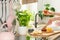 Woman`s hands holding a breakfast French bread roll and spreading fruit jam in a white kitchen interior with pink elements and he