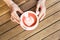 Woman`s hands holding cup of cappuccino on wooden table. Colored in coral color foam