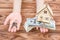 Woman`s hands holding money, model of house and keys of house in palms over wooden table