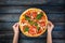 Woman`s hands holding a perfect pizza margarita with tomato slices, olives and basil leaves. Top view