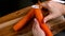 Woman`s hands peeling fresh carrot above a wooden board close up