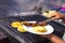 Woman\\\'s hands serving arepas with cheese and chorizo on a plate next to the grill