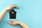 Woman`s hands surround a mock-up of a dark house on a blue background. Family, real estate and insurance concept, flat lay, top