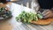 A woman's hands use a kitchen knife to cut lettuce leaves on a wooden board.