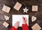 Woman`s hands writing christmas letter on paper on wooden background with gifts and decorations