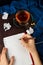 Woman`s hands writting in a notebook with blank page with cramped paper, glasses and cup of tea or coffee