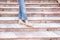 Woman`s legs in blue twisted jeans and in beige boots on pink marble staircase. Front view