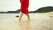 Woman`s legs close up. The ocean on a background. The woman in a red dress walks on the beach. Closeup of beautiful girl