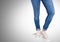 Woman`s legs in jeans in front of grey background