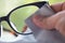 Woman`s right hand cleaning grey shortsighted or nearsighted eyeglasses by grey microfibre cleaning cloths, Bokeh green backgroun
