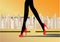 Woman`s slender legs in red high-heeled shoes walk on the road against the yellow background skyscrapers