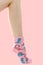 Woman`s unshaven leg in pink socks with dinosaurs on a pink background. Pink flowers is in the socks