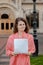 A woman sadly holds securities in her hands, standing next to the university