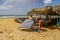 woman salesman on beach trades with a tourist in a hat and bikini on the shore of the sandy ocean among gazebos and