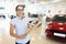 Woman salesman with clipboard in her hands showing new car in dealership