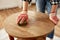 woman sanding old round wooden table with sponge