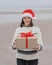 woman in a Santa Claus hat with a gift box in her hands smiles. a happy European woman carries a gift for New Year or