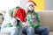 Woman in santa claus hat holds her head with hands while friend in protective mask speaks on phone