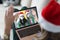 Woman in santa claus hat holds laptop on knees and communicates with her friends in protective masks on face portrait