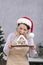 Woman in Santa hat holds gingerbread house and tries to take bite. Vertical frame