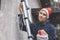 Woman with santa hat standing on ladder outdoors and installing christmas lights and decors on house facade