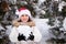 A woman in Santa's hat holds a snowball in her hands in a snow-covered winter forest, a place for text