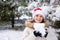 A woman in Santa's hat holds a snowball in her hands in a snow-covered winter forest, a place for text