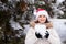 A woman in Santa's hat holds a snowball in her hands in a snow-covered winter forest, a place for text